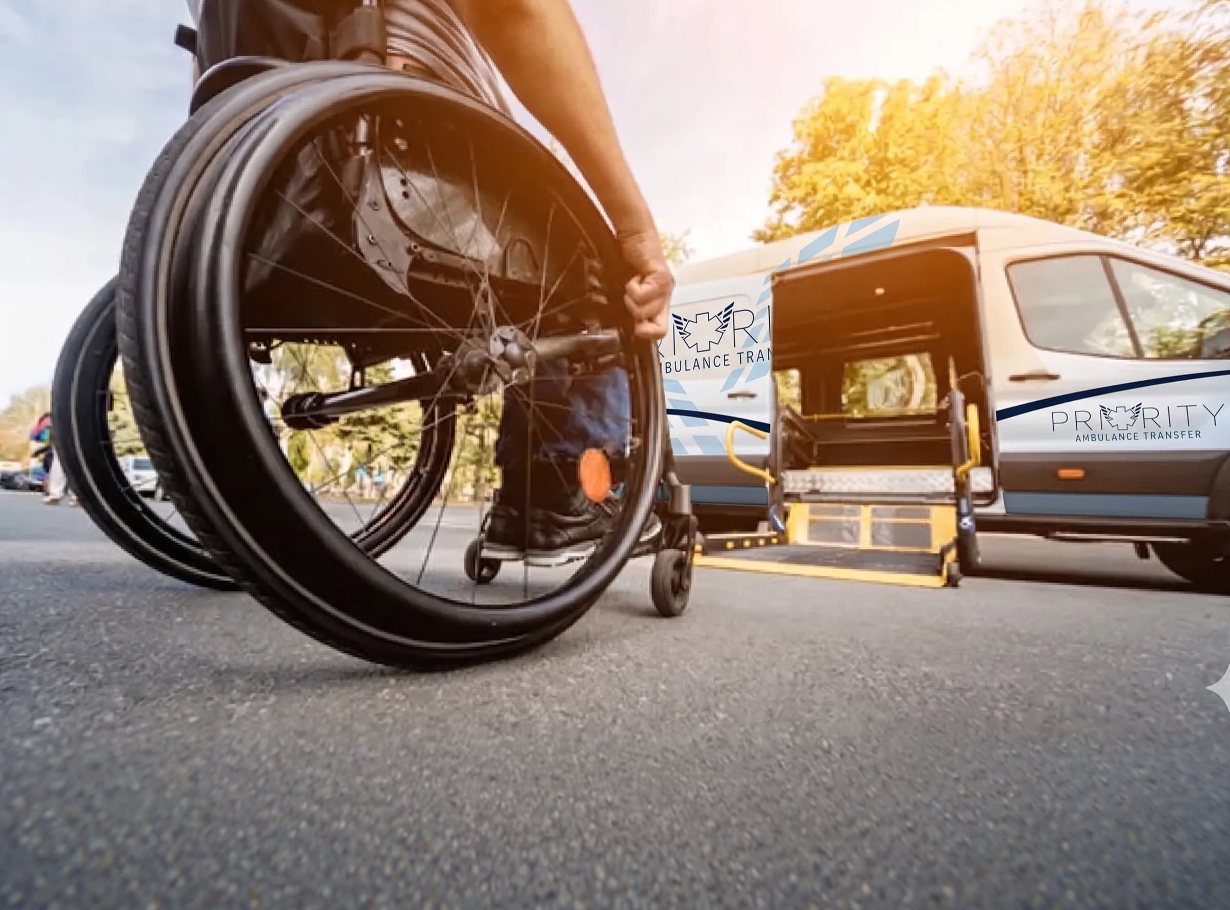 A passenger using a wheelchair next to a Priority Ambulance Transfer wheelchair-accessible van.